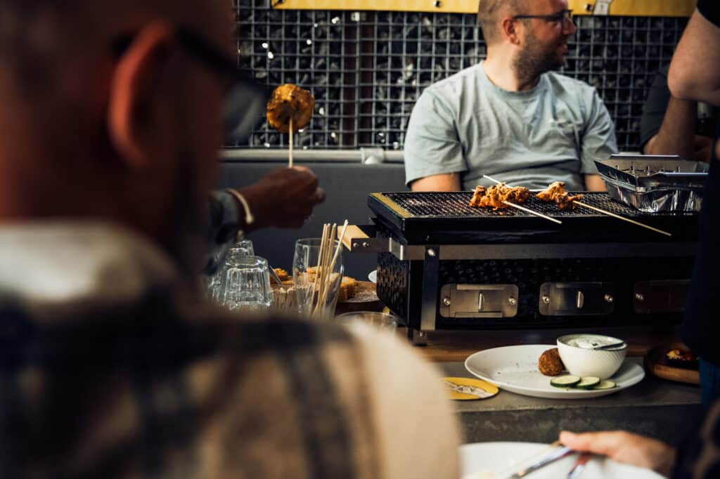 Mensen bereiden saté op tafelgrill tijdens diner