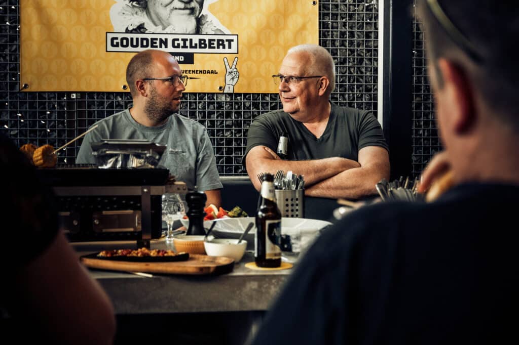 Twee mannen praten aan tafel met eten en drinken.